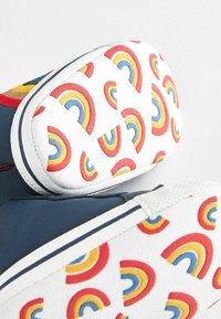 Chaussures en textile avec une base bleu marine et une partie supérieure blanche ornée de motifs colorés en arc-en-ciel rouges, jaunes et bleus.