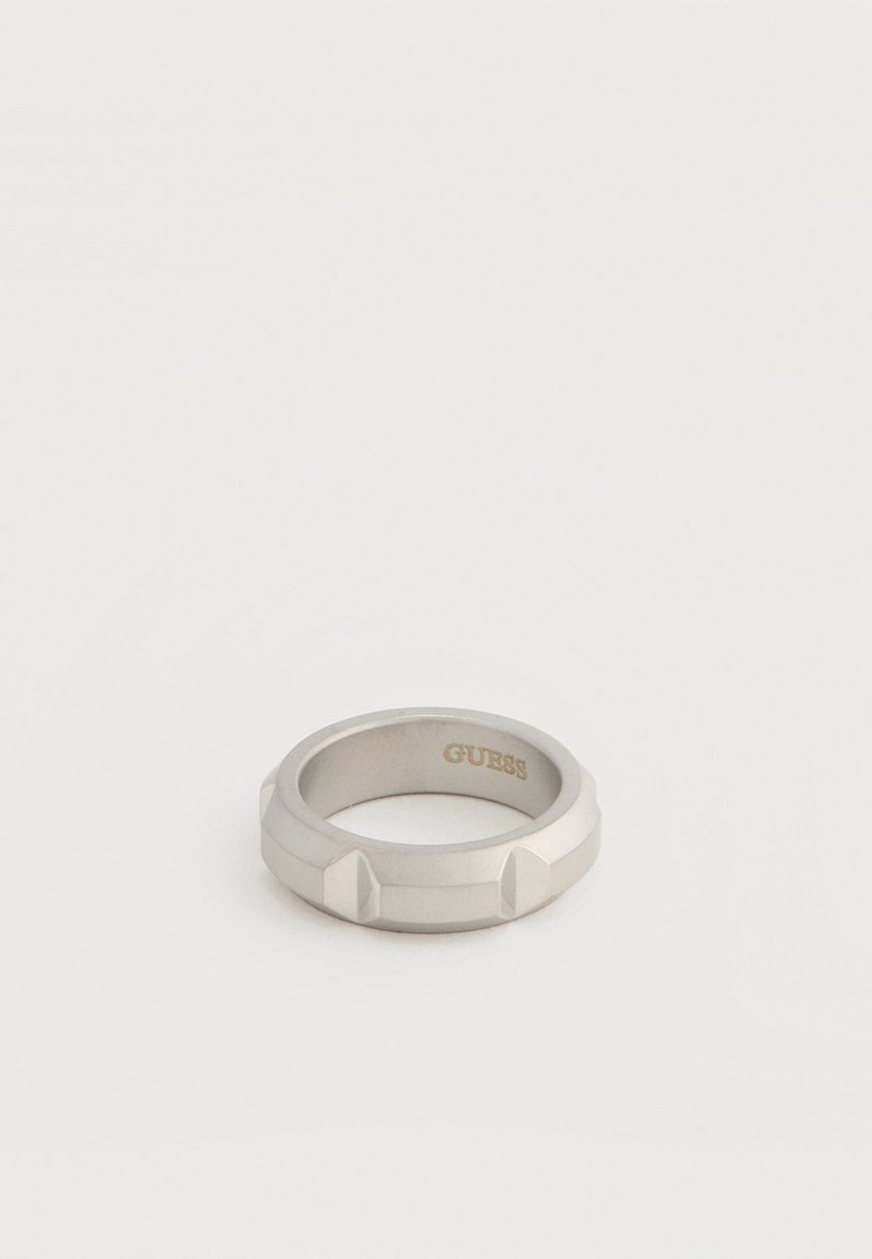 Bague en métal argenté avec des accents rectangulaires en relief autour du bracelet et "GUESS" gravé à l'intérieur de la surface intérieure.