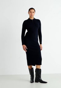 Black long-sleeve dress with a polo collar, fitted design, mid-calf length, paired with tall black cowboy boots. Smooth knit texture.