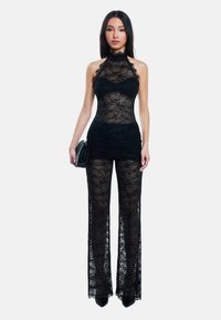 Zwarte kanten bodysuit met hoge halslijn, versierd met bloemenpatronen en een aansluitende taille, gecombineerd met flared kanten broeken. Zwarte hakken en een clutch.