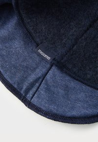Mørkeblå hatt med en teksturert ulloverdel og glatt denimlignende nedre del, som har et fremtredende "maximo"-merke langs sømmen.