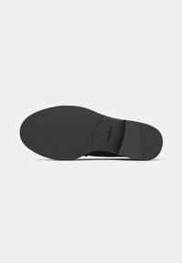 Semelle de chaussure noire en matériau caoutchouteux texturé, de forme courbée, avec le logo "ALDO" embossé près du talon. Design simple et plat.