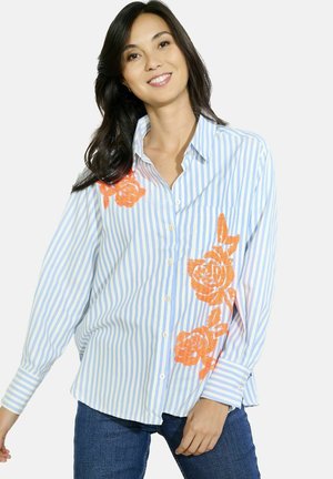 Camisa de botones a rayas azul claro y blanca con gran bordado floral naranja en el lado izquierdo, con corte relajado y mangas largas.