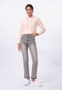 Haut à capuche court couleur pêche clair avec une texture en chevrons, associé à un jean droit gris avec un ourlet effiloché et des chaussures blanches à enfiler.