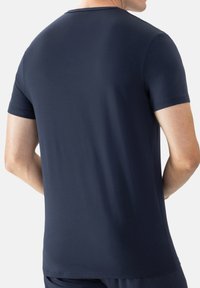 Uomo che indossa una maglietta casual blu navy a maniche corte, visto da dietro, su uno sfondo bianco uniforme.