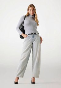 Pull à col roulé gris, jean large à délavage clair, et escarpins noirs à talons aiguilles. Sac à main noir avec bandoulière.