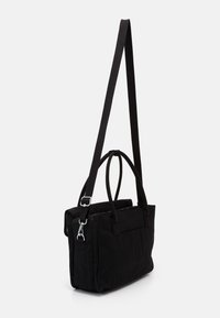 Sort stof tote tas med doble top håndtag og en aftagelig skulderrem. Har en blød tekstur og lynlåslukning.