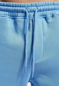 Helle blaue Jogginghosen aus weichem Stoff verfügen über einen elastischen Bund mit Kordelzug, eine Seitentasche und eine glatte Textur.
