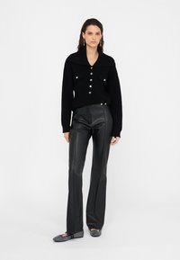 Maglione nero a maglia con un grande colletto e chiusura a bottoni frontale, abbinato a pantaloni neri in ecopelle a vita alta. Design strutturato e aderente.