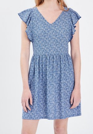 Woman wearing a blue floral short dress with ruffled cap sleeves and a gathered waist against a plain background.