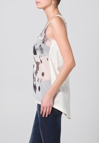 Top sans manches avec un motif abstrait gris et noir sur un tissu transparent ; dos uni blanc ; coupe décontractée ; ourlet arrondi visible.