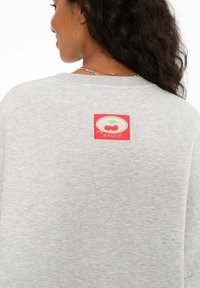 Sivé mikina s okrúhlym výstrihom. Na zadnej strane má červenú a zelenú značku s grafikou čerešní a je vyrobená z mäkkej textúrovanej látky.