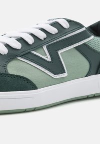 Sneakers with a mix of dark green leather and light green fabric. White laces and stitching. Rubber sole with textured accents.