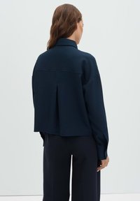 Navy textured blouse with a cropped cut, featuring a back pleat and long sleeves, paired with tailored dark trousers.