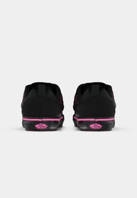 Et par svarte Vans-sko med rosa detaljer sett fra baksiden, som viser "Vans Off The Wall" logoen på hælen.