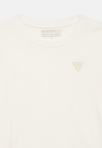 Κρεμ μπλουζάκι με στρογγυλή λαιμόκοψη και μικρό ανάγλυφο τριγωνικό λογότυπο στην αριστερή πλευρά του στήθους. Κανονική εφαρμογή.