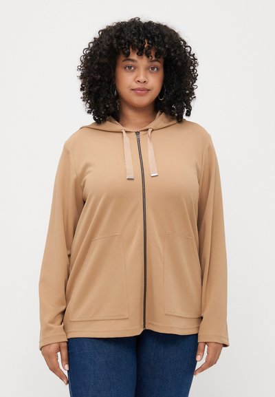 Hoodie zippé marron clair en matériau doux, avec une capuche, deux poches avant et des cordons de serrage en acier inoxydable.