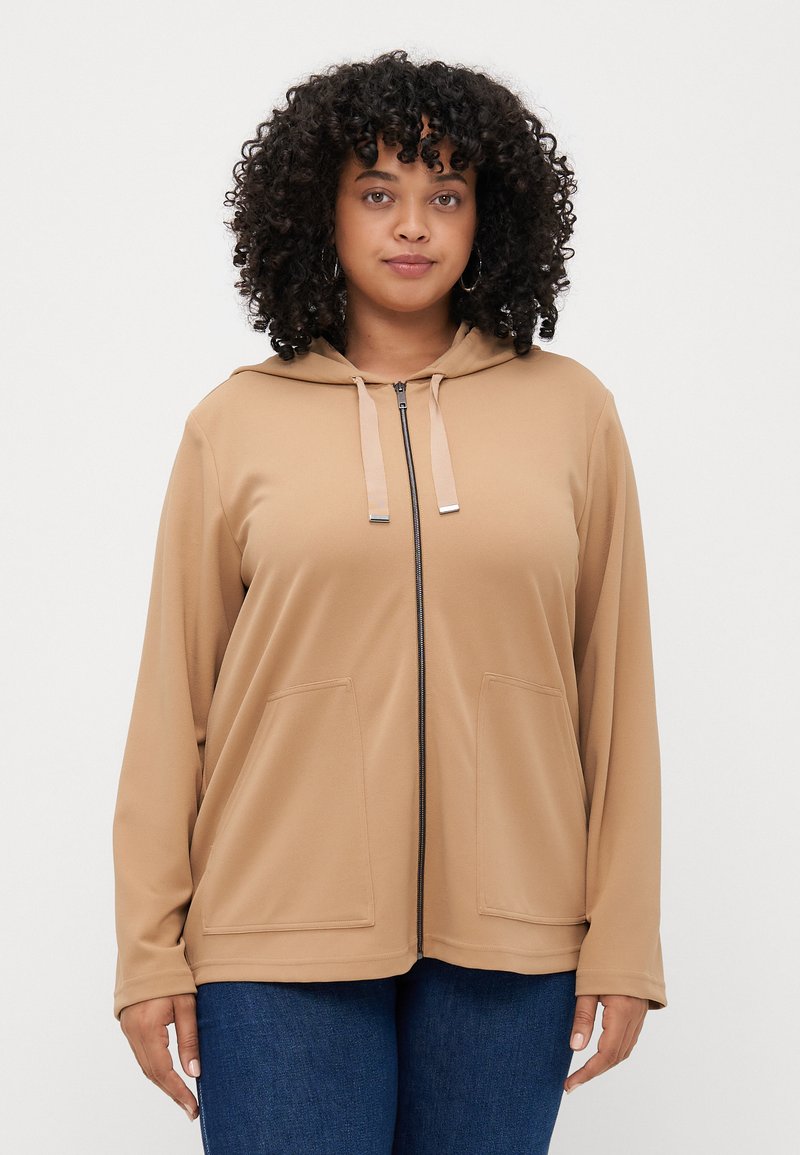 Φωτεινό καφέ φούτερ με φερμουάρ, φτιαγμένο από μαλακό υλικό, που διαθέτει κουκούλα, δύο μπροστινές τσέπες και κορδόνια με ασημί λεπτομέρειες.