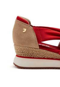 Sandalia cuña roja y beige con suela de yute trenzado, que presenta un upper liso y un pequeño logotipo dorado en la zona del tacón.