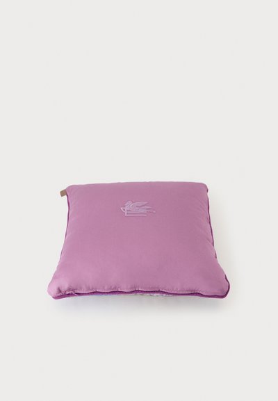 Coussin carré violet avec un logo subtil d’animal ailé brodé au centre, sur fond blanc uni.