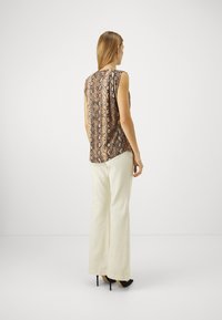 Top senza maniche con motivo serpente marrone e nero, abbinato a pantaloni larghi color avorio e tacchi neri. Tessuto morbido e vestibilità comoda.