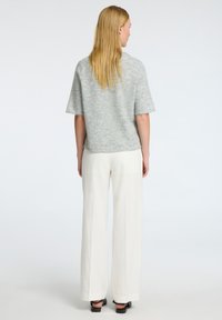 Maglione grigio chiaro a maniche corte realizzato in materiale morbido, abbinato a pantaloni bianchi a gamba larga e sandali neri, vista da dietro.