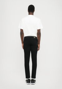 Μαύρα τζιν με slim fit, φτιαγμένα από τζιν ύφασμα, με μια πίσω τσέπη που έχει λογότυπο. Φορεμένα με λευκό T-shirt και μαύρα παπούτσια.