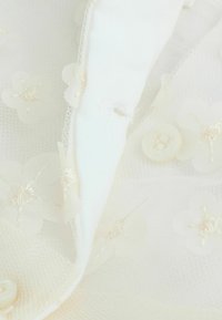 Tessuto bianco con un motivo in pizzo floreale, caratterizzato da fiori ricamati e un dettaglio a bottone. Texture morbida, elementi di design delicati.