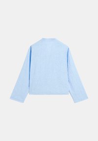 Chemise à manches longues bleu clair, fabriquée en tissu texturé, présente un col haut et une coupe décontractée avec des coutures d'épaule abaissées.