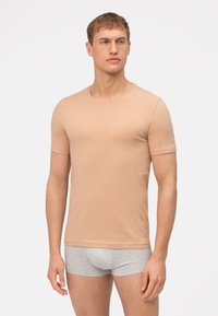 Beige T-shirt met korte mouwen van zachte stof en een ronde hals. Heeft een getailleerde snit en een subtiele logo-accent op de mouw.