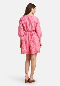 Rotes Baumwollkleid mit Dreiviertelärmel, tailliertem Schnitt und ausgestellt Rock. Mit floralen Stickereien in kontrastierender Farbe.