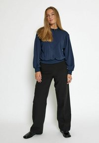 Navy blue sweatshirt with a V-shaped design, combined with high-waisted black trousers, featuring a smooth texture and fitted silhouette.