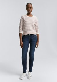 Randig rosa och vit långärmad tröja i kombination med mörkblå slim-fit jeans och vita sneakers. Slät textur med ribbade muddar.