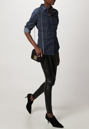 Dunkelblaues Denim-Hemd mit gepunktetem Muster, hochgekrempelten Ärmeln, kombiniert mit schwarzen Leder-Skinny-Hosen und schwarzen Wildleder-High Heels.