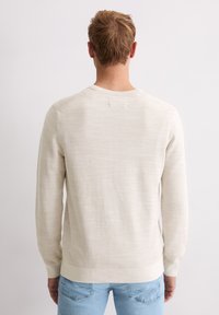 Jasnobeżowy dzianinowy sweter z długimi rękawami i okrągłym dekoltem. Posiada wzór fakturowany z gładkim wykończeniem oraz ściągacz w pasie.