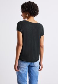 Haut noir à manches courtes avec un col rond et une coupe décontractée, présentant une texture subtile et un détail de couture à l'arrière. Associé à un jean bleu clair.