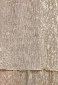 Gros plan sur un tissu beige superposé avec des fils métalliques verticaux créant une surface brillante, texturée et un motif côtelé subtil.
