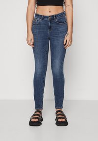 Tight jeans i mørkeblå denim, knaplukning, forlommer og en falmet tekstur. Kombineret med sorte sandaler med remme.