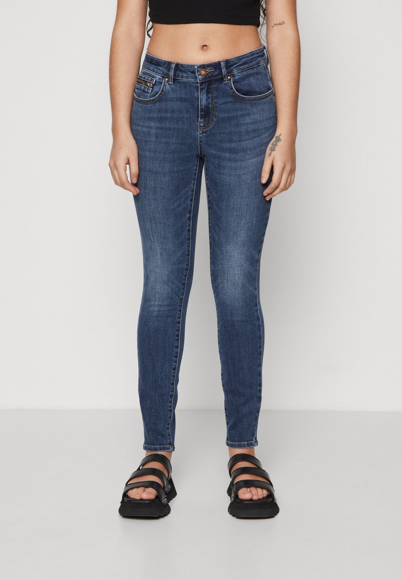 Tight jeans i mørkeblå denim, knaplukning, forlommer og en falmet tekstur. Kombineret med sorte sandaler med remme.