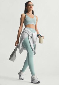 Light blue sports bra and matching leggings with white logo, paired with a gray sweatshirt tied at the waist and white sneakers.