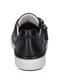 Chaussure en cuir noire avec un dos arrondi, semelle blanche, fermeture éclair sur le côté et finition texturée près du talon. Logo sur la semelle.