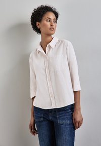 Light pink button-up shirt with a collar, three-quarter sleeves, and a front pocket, paired with dark blue denim jeans.
