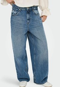 Široké modré džíny z denimu s vybledlým vzhledem, obsahující přední kapsy a vysoký pas. Materiál je měkký a texturovaný.