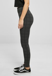 Leggings taille haute et ajustés, avec un motif pied-de-poule texturé en noir et gris, accompagnés de baskets noires ornées d'accents blancs.