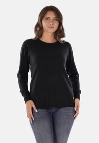 Maglione nero a maniche lunghe con scollatura rotonda, polsini e orlo a costine. Presenta un piccolo dettaglio del logo nella parte inferiore. Tessuto con una consistenza liscia.