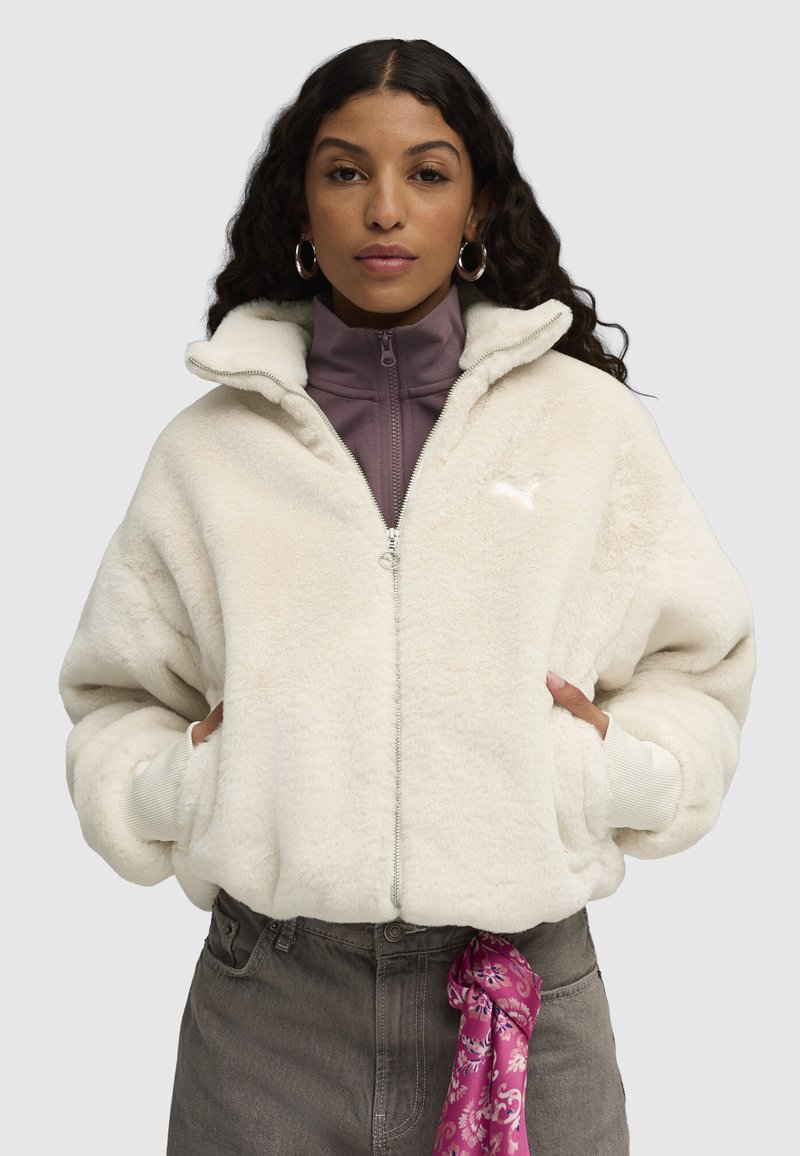 White fluffy zip-up jacket with a high collar, featuring a soft texture and ribbed cuffs, layered over a purple high-neck top.