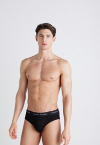 Schwarze Baumwollslips mit einem Logo-Bund, slim-fit Design und glatter Textur, getragen von einem Model vor einem neutralen Hintergrund.