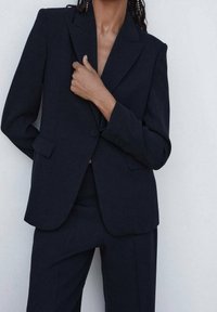 Blazer ajustado de marinero con solapas de muesca, cierre de un botón y bolsillos frontales. Textura mate con silueta estructurada y diseño entallado.