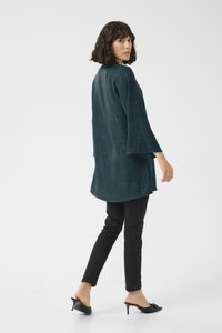 Dlouhý rukáv, texturovaný tyrkysový kimono kabát, v kombinaci s černými slim-fit kalhotami a sandály na otevřenou špičku, pohled zezadu.
