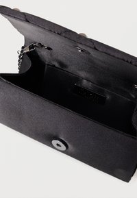 Μαύρη τσάντα χειρός με λεία υφή, κλείσιμο τύπου snap και αλυσίδα ως λουράκι. Ο εσωτερικός της χώρος είναι ευρύχωρος με μια διακριτική επώνυμη ετικέτα.